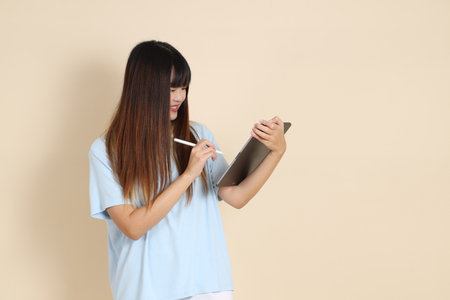 Young Asian woman wearing a light blue polo shirt, and white shorts, Holding tablet against a plain beige background. College student, Gen Z, Summerの写真素材