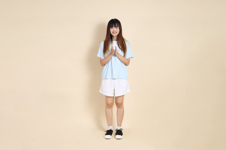 Young Asian woman wearing a light blue polo shirt, and white shorts, claping hands against a plain beige background. College student, Gen Z, Summerの写真素材