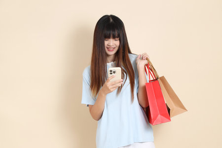 Young Asian woman wearing a light blue polo shirt, and white shorts, holding shopping bag against a plain beige background. College student, Gen Z, Summerの写真素材