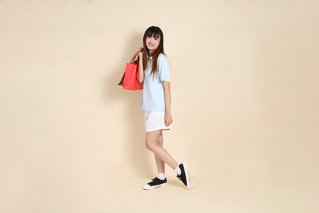 Young Asian woman wearing a light blue polo shirt, and white shorts, holding shopping bag against a plain beige background. College student, Gen Z, Summerの写真素材