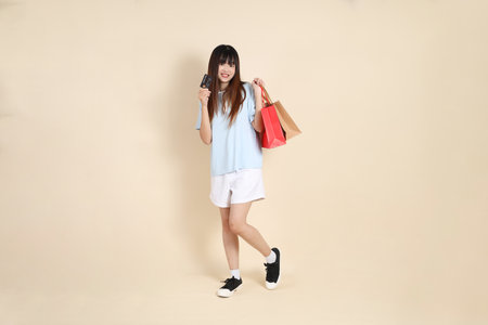 Young Asian woman wearing a light blue polo shirt, and white shorts, holding shopping bag against a plain beige background. College student, Gen Z, Summerの写真素材