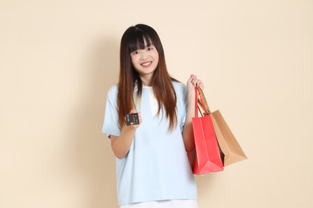 Young Asian woman wearing a light blue polo shirt, and white shorts, holding shopping bag against a plain beige background. College student, Gen Z, Summerの写真素材