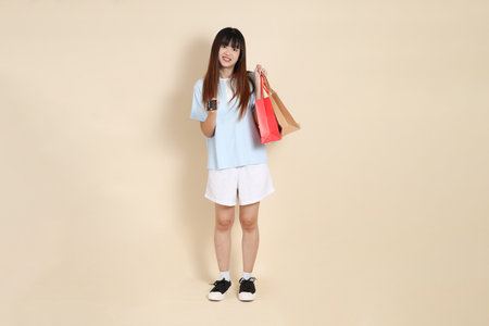 Young Asian woman wearing a light blue polo shirt, and white shorts, holding shopping bag against a plain beige background. College student, Gen Z, Summerの写真素材