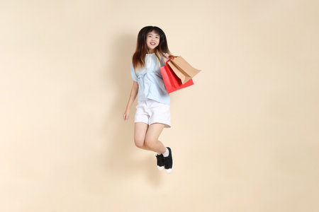 Young Asian woman wearing a light blue polo shirt, and white shorts, holding shopping bag against a plain beige background. College student, Gen Z, Summerの写真素材