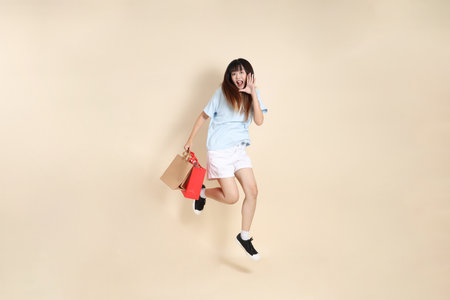 Young Asian woman wearing a light blue polo shirt, and white shorts, holding shopping bag against a plain beige background. College student, Gen Z, Summerの写真素材