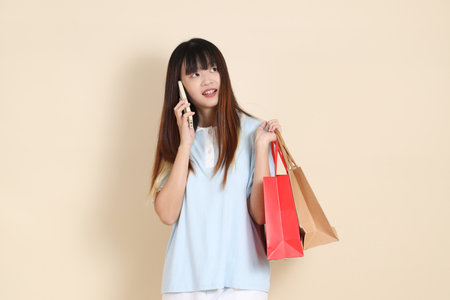 Young Asian woman wearing a light blue polo shirt, and white shorts, holding shopping bag against a plain beige background. College student, Gen Z, Summerの写真素材