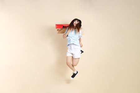 Young Asian woman wearing a light blue polo shirt, and white shorts, holding shopping bag against a plain beige background. College student, Gen Z, Summerの写真素材