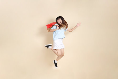 Young Asian woman wearing a light blue polo shirt, and white shorts, holding shopping bag against a plain beige background. College student, Gen Z, Summerの写真素材