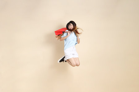 Young Asian woman wearing a light blue polo shirt, and white shorts, holding shopping bag against a plain beige background. College student, Gen Z, Summerの写真素材