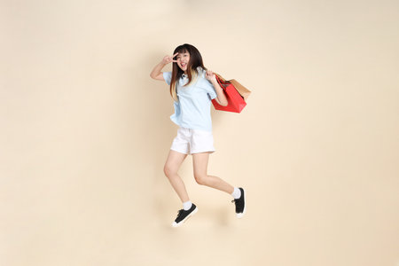 Young Asian woman wearing a light blue polo shirt, and white shorts, holding shopping bag against a plain beige background. College student, Gen Z, Summerの写真素材
