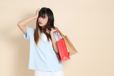 Young Asian woman wearing a light blue polo shirt, and white shorts, holding shopping bag against a plain beige background. College student, Gen Z, Summerの写真素材
