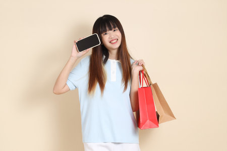 Young Asian woman wearing a light blue polo shirt, and white shorts, holding shopping bag against a plain beige background. College student, Gen Z, Summerの写真素材