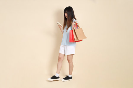 Young Asian woman wearing a light blue polo shirt, and white shorts, holding shopping bag against a plain beige background. College student, Gen Z, Summerの写真素材