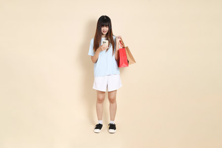 Young Asian woman wearing a light blue polo shirt, and white shorts, holding shopping bag against a plain beige background. College student, Gen Z, Summerの写真素材
