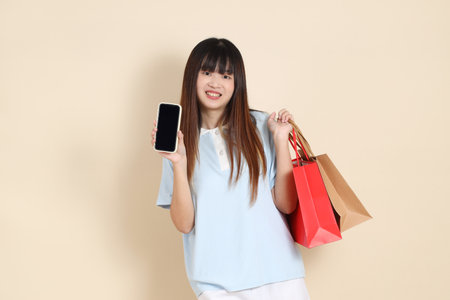 Young Asian woman wearing a light blue polo shirt, and white shorts, holding shopping bag against a plain beige background. College student, Gen Z, Summerの写真素材