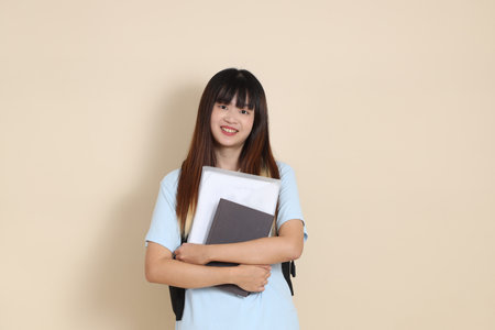 Asian woman wearing blue polo shirt, carrying school backpack, holding a book against a plain beige background. Gen Z,の写真素材