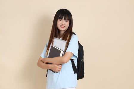 Asian woman wearing blue polo shirt,  white shorts, carrying school backpack, holding a book against a plain beige background. Gen Z,の写真素材
