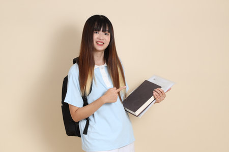 Asian woman wearing blue polo shirt,  white shorts, carrying school backpack, holding a book against a plain beige background. Gen Z,の写真素材