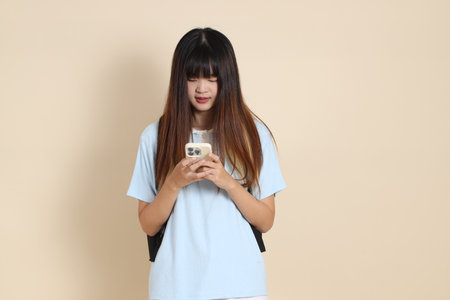 Asian woman wearing blue polo shirt,  white shorts, carrying school backpack, Holding mobile phone against a plain beige background. Gen Z,の写真素材