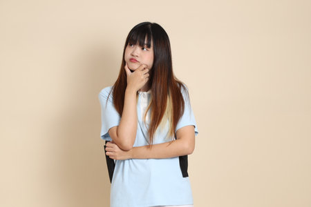 Asian woman wearing blue polo shirt,  white shorts, carrying school backpack, holding a book against a plain beige background. Gen Z,の写真素材