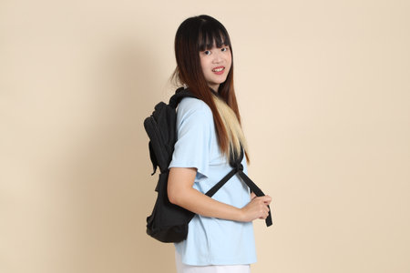 Asian woman wearing blue polo shirt,  white shorts, carrying school backpack, holding a book against a plain beige background. Gen Z,の写真素材