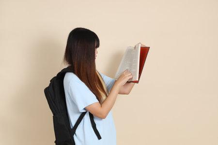 Asian woman wearing blue polo shirt,  white shorts, carrying school backpack, holding a book against a plain beige background. Gen Z,の写真素材