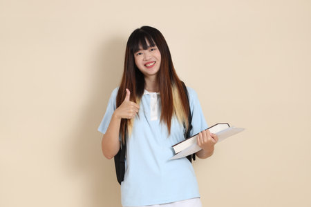 Asian woman wearing blue polo shirt,  white shorts, carrying school backpack, holding a book against a plain beige background. Gen Z,の写真素材