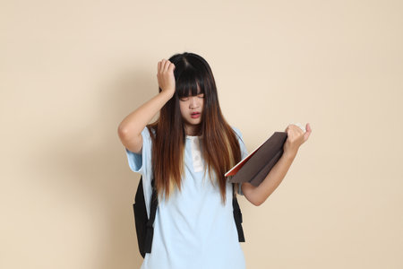 Asian woman wearing blue polo shirt,  white shorts, carrying school backpack, holding a book against a plain beige background. Gen Z,の写真素材