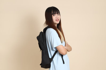Asian woman wearing blue polo shirt, carrying school backpack against a plain beige background.の写真素材