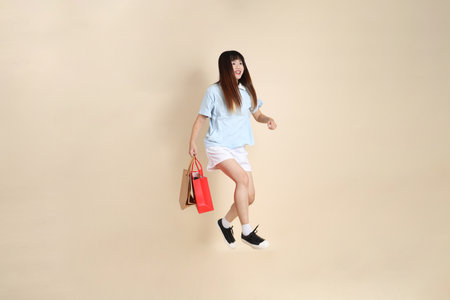 Young Asian woman wearing a light blue polo shirt, and white shorts, holding shopping bag against a plain beige background. College student, Gen Z, Summerの写真素材