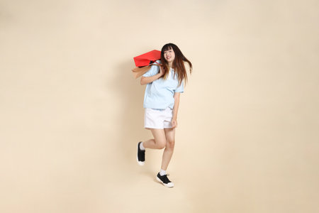 Young Asian woman wearing a light blue polo shirt, and white shorts, holding shopping bag against a plain beige background. College student, Gen Z, Summerの写真素材