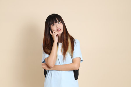 Asian woman wearing blue polo shirt, carrying school backpack against a plain beige background.の写真素材