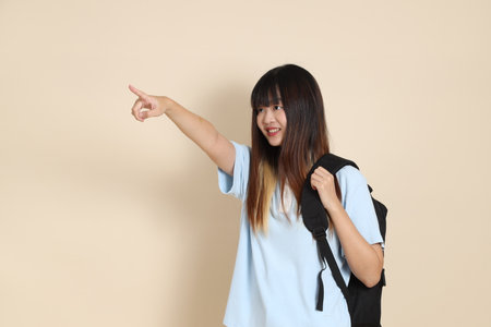 Asian woman wearing blue polo shirt, carrying school backpack against a plain beige background.の写真素材
