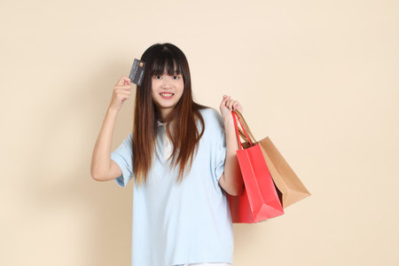 Young Asian woman wearing a light blue polo shirt, and white shorts, holding shopping bag against a plain beige background. College student, Gen Z, Summerの写真素材