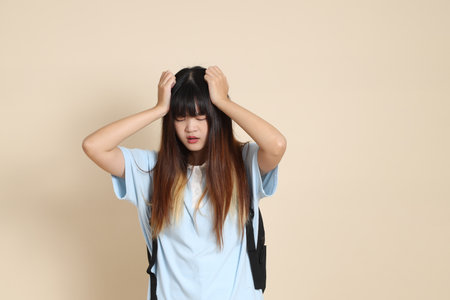 Asian woman wearing blue polo shirt, carrying school backpack, holding a book against a plain beige background. Gen Z,の写真素材