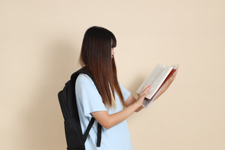 Asian woman wearing blue polo shirt, carrying school backpack, holding a book against a plain beige background. Gen Z,の写真素材