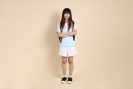 Asian woman wearing blue polo shirt,  white shorts, carrying school backpack, holding a book against a plain beige background. Gen Z,の写真素材