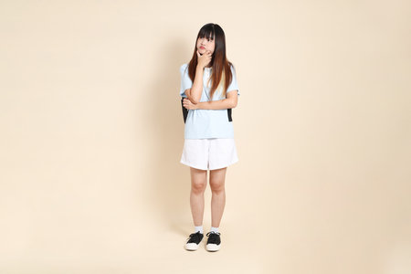 Asian woman wearing blue polo shirt, white shorts, carrying school backpack against a plain beige background.の写真素材