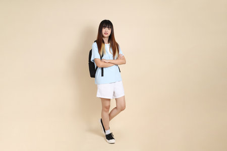 Asian woman wearing blue polo shirt,  white shorts, carrying school backpack, holding a book against a plain beige background. Gen Z,の写真素材