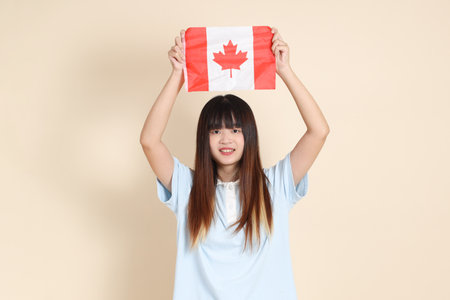 Young Asian woman wearing a light blue polo shirt, and white shorts, holding canadian or canada flag against a plain beige background. College student, Gen Z, Summerの写真素材