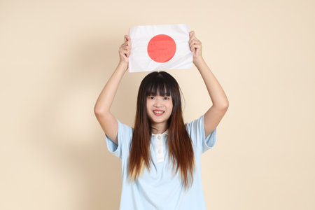 Young Asian woman wearing a light blue polo shirt, and white shorts, holding japanese or japan flag against a plain beige background. College student, Gen Z, Summerの写真素材