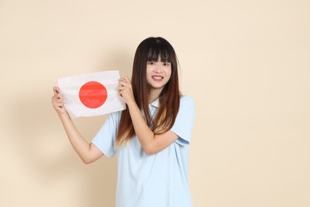 Young Asian woman wearing a light blue polo shirt, and white shorts, holding japanese or japan flag against a plain beige background. College student, Gen Z, Summerの写真素材