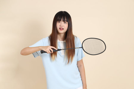 Young Asian woman wearing a blue polo shirt, and white shorts, playing badminton or holding...
