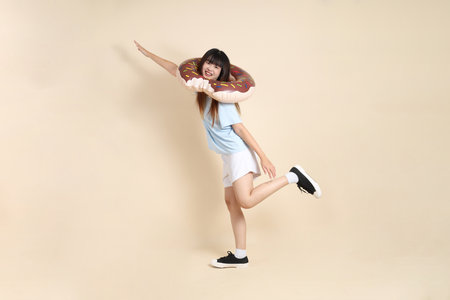 Smiling young Asian woman wearing sunglasses on head, holding a donut inflatable swim ring against beige background. Summer holiday, vacation, College student, Gen Zの写真素材