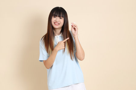 Young Asian woman wearing a light blue polo shirt, and white shorts, holding a pen a plain beige background. College student, Gen Z, Summerの写真素材