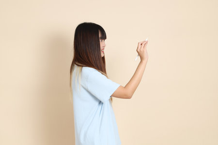 Young Asian woman wearing a light blue polo shirt, and white shorts, holding a pen a plain beige background. College student, Gen Z, Summerの写真素材