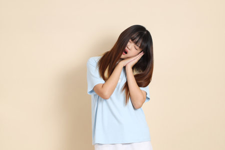 Young Asian woman wearing a light blue polo shirt, and white shorts, Sleepy or yawn against a plain beige background. Summerの写真素材