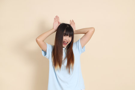 Medium shot of a young Asian woman wearing a light blue polo shirt, and white shorts, Silly and funny against a plain beige background. College student, Gen Zの写真素材