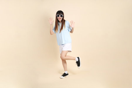 Asian woman wearing a blue polo shirt, white shorts, , sunglasses, dancing a beige background. College student, Gen Z, Summerの写真素材