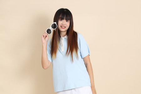 Asian woman wearing a blue polo shirt, white shorts, sunglasses, standing and smiling against a...